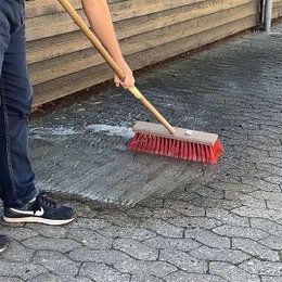 Gade kost med langt skaft til fliser Person fejer terrassefliser med rød gade kost