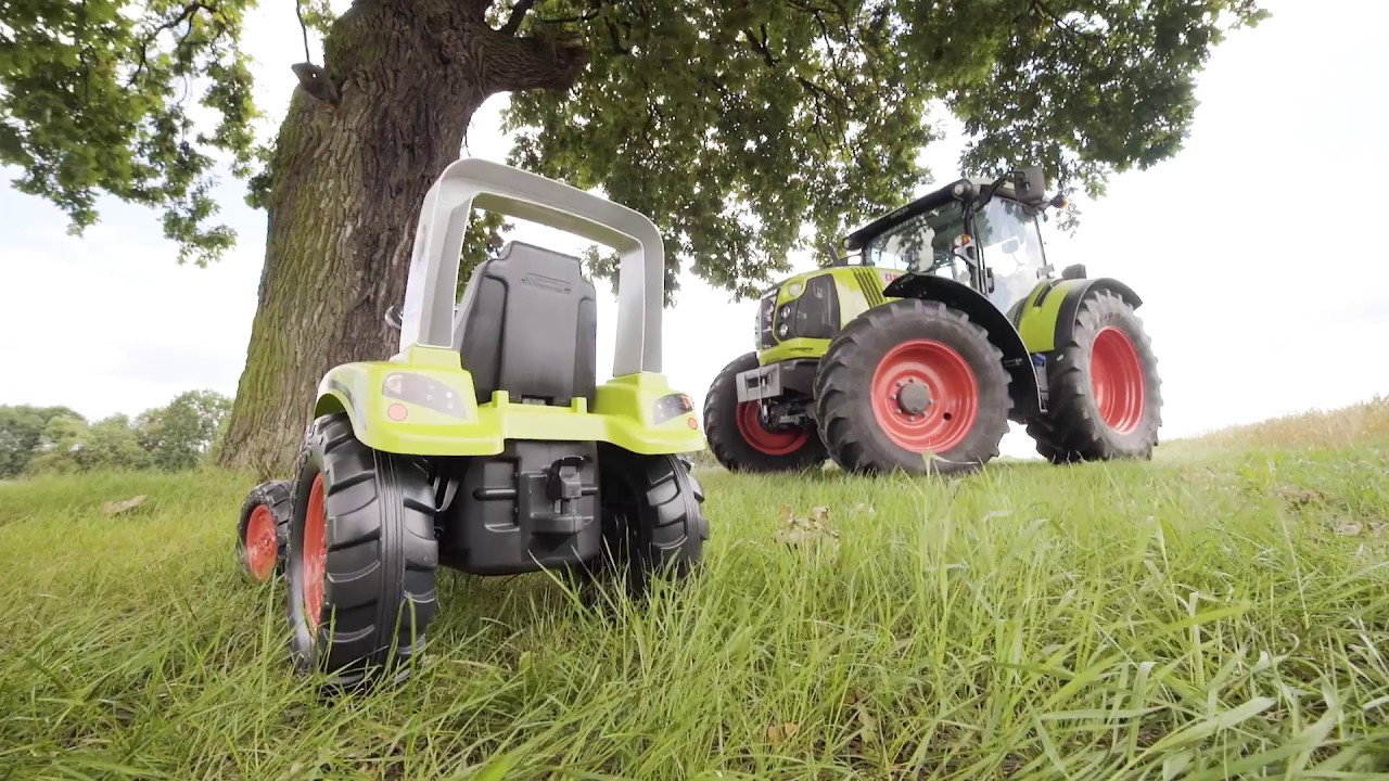 Claas pedaltraktor inkl. vogn - FALK Arion 430 replika, til børn 3-7 år, lavet i Frankrig Grøn Claas pedaltraktor med tilhørende vogn foran en stor traktor på græs - FALK pedalreplika af Claas Arion 430, robust udendørs legetøj til børn 3-7 år, 100% fremstillet i Frankrig
