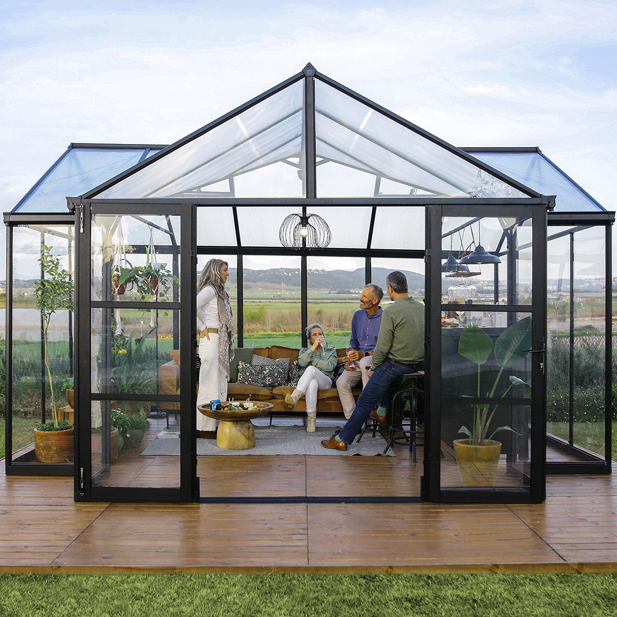 Palram Canopia Triumph orangeri 16,00 m² i antracitgrå med sort pulverlakeret aluminiumsramme og klare polycarbonatpaneler; stilfuldt T-formet orangeri med terrassegulv, planter og personer, velegnet til have, plantehygge og udendørsliv