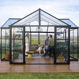 Palram Canopia Triumph orangeri 16,00 m² - antracitgrå orangeri med pulverlakeret aluminiumramme Palram Canopia Triumph orangeri 16,00 m² i antracitgrå med sort pulverlakeret aluminiumsramme og klare polycarbonatpaneler; stilfuldt T-formet orangeri med terrassegulv, planter og personer, velegnet til have, plantehygge og udendørsliv