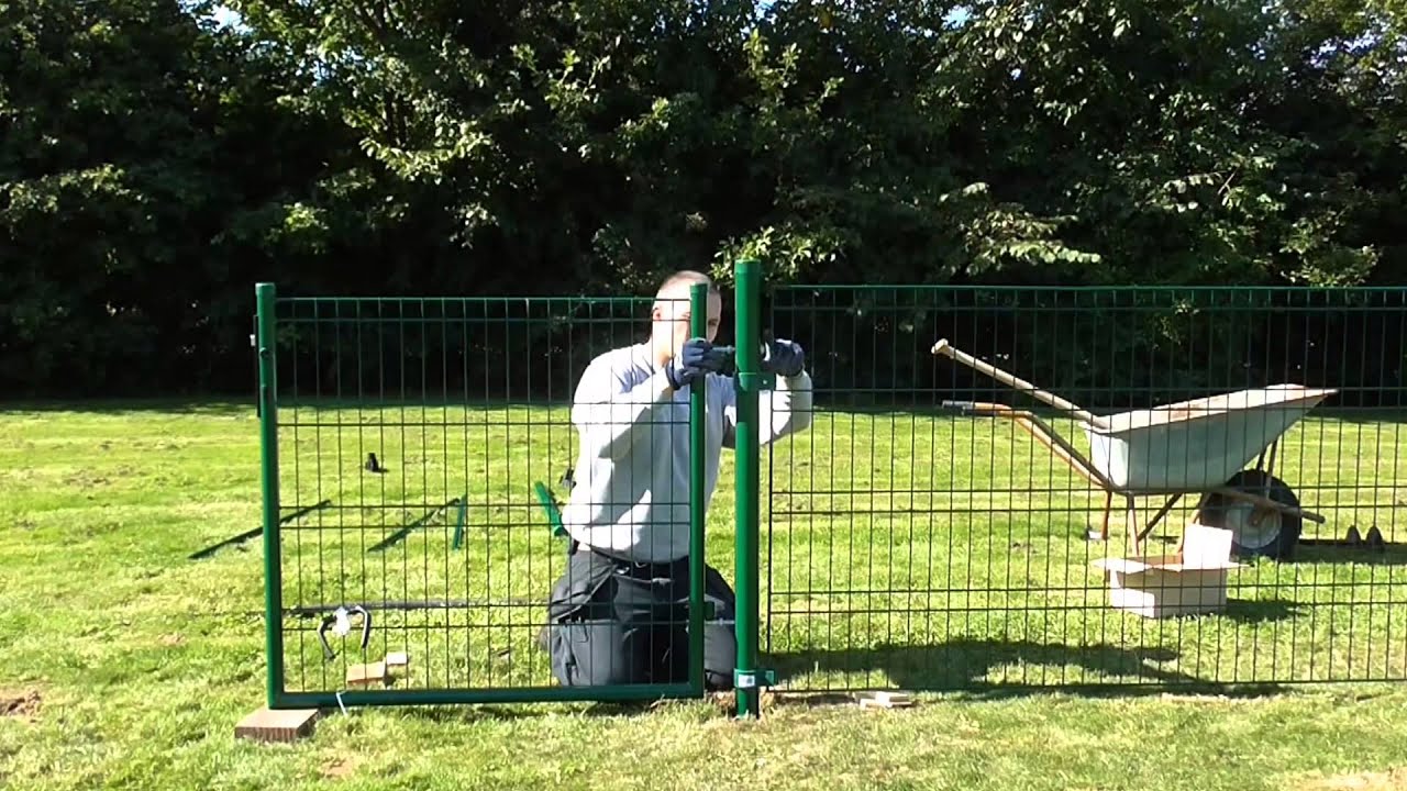 Montering af Hortus Panelhegn hegnspakke 8 fag i grøn; person sætter et grønt panel op på græsplæne ved hjælp af stolpe, med trillebør og værktøj i baggrunden