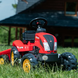 Rød pedaltraktor til børn i haven Rød legetøjs-pedaltraktor til børn på græs