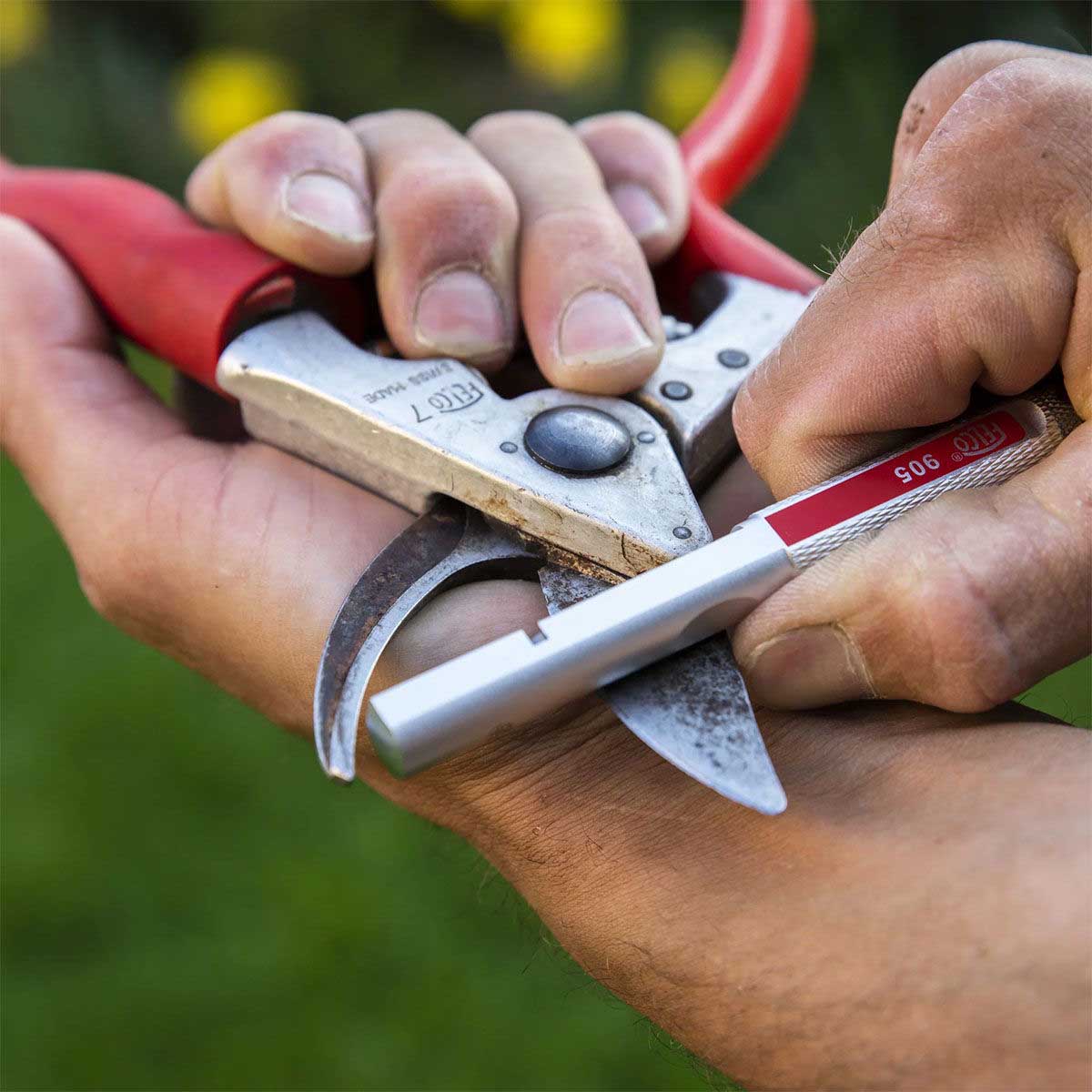 Havearbejder sliber beskærersaks med slibestift