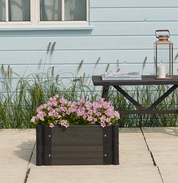 Sort plantekasse til terrasse og altan Rektangulær sort plantekasse med lyserøde blomster