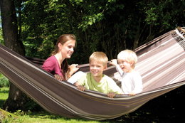 Familiehygge i hængekøje i haven Kvinde og to børn leger i brun hængekøje i have