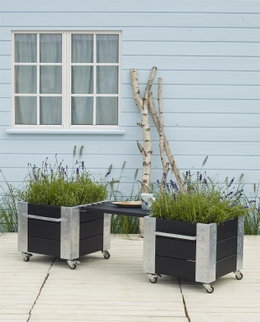 Rullekasser med planter og bord til terrasse To plantekasser på hjul med bord foran husvæg