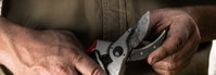 Sekatør til beskæring holdt i hænderne Hænder tæt på, der holder en metal sekatør med rødt håndtag og slidt klinge, klar til havebeskæring