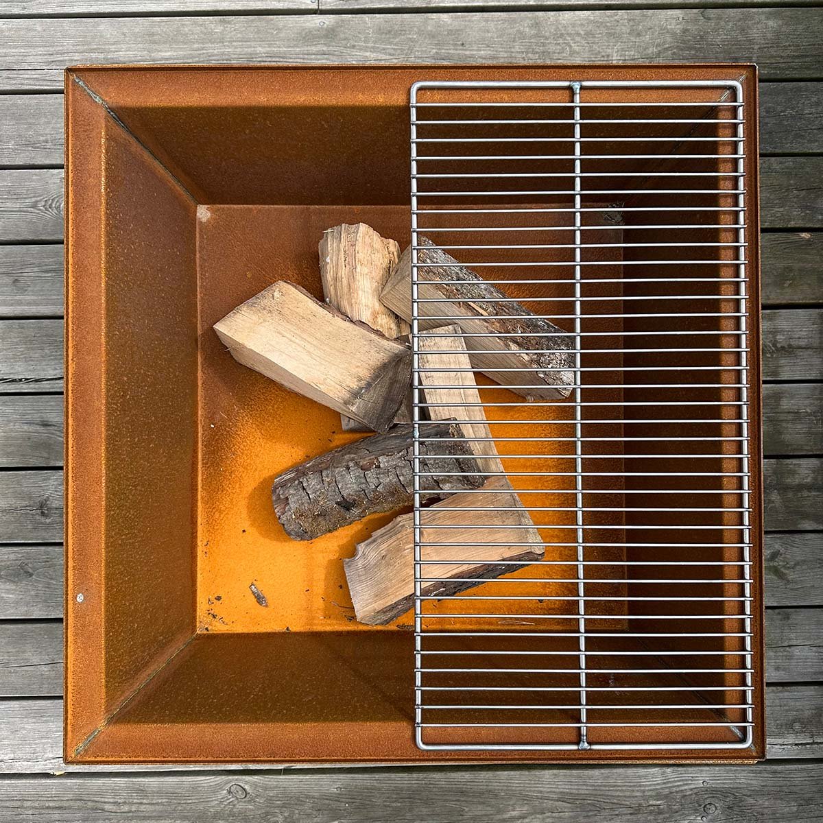 Firkantet ildsted i cortenstål med grillrist Firkantet cortenstål-bålsted med grillrist og brænde