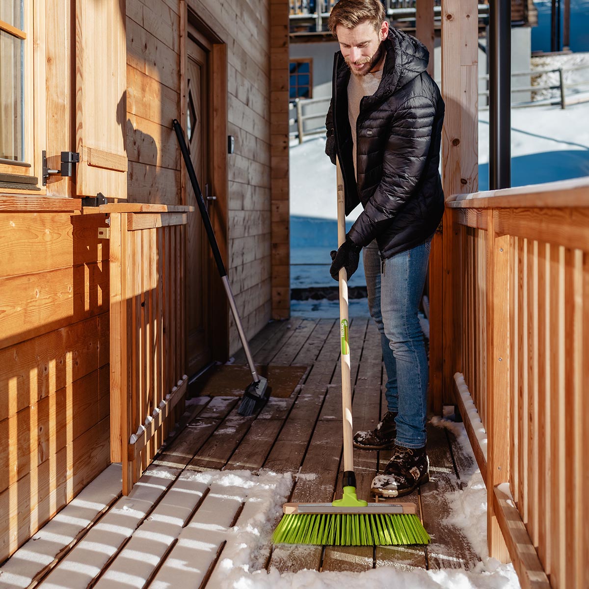 Fejning af sne på træveranda med Freund Trækost 156 cm; diagonalt placerede grønne ELASTON-børster, integreret skrabekant, robust plastfastgørelse og FSC-certificeret træskaft – arbejdsbredde 46 cm, til indendørs og udendørs brug