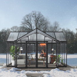 Palram Canopia Triumph orangeri 16,00 m2 antracitgrå – T-formet orangeri med pulverlakeret aluminiumsramme og klare polycarbonatpaneler Canopia by Palram Triumph orangeri 16,00 m² i antracitgrå, T-formet pulverlakeret aluminiumsramme med klare akryl- og polycarbonatpaneler; indrettet som hyggelig vinterstue med sofa, planter og varmelampe i en snedækket have