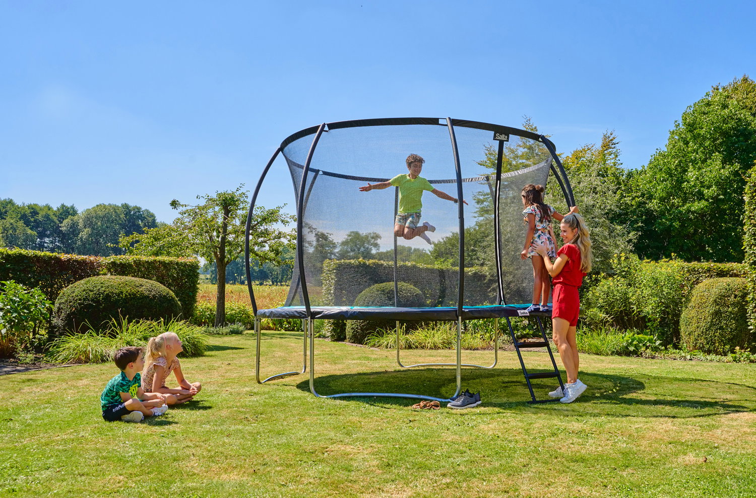 Børn leger på stor trampolin med net i haven