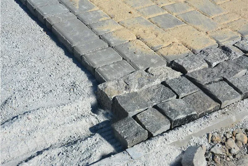 Grå granitbrosten og kantsten til belægning – fliser lagt på sand- og stabilgrus Nærbillede af grå granitbrosten og kantsten under lægning på sand- og stabilgruslag