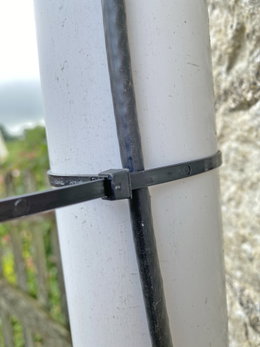Sort kabelbinder til fastgørelse udendørs Sort strips, der fastgør kabel til rund hvid stolpe