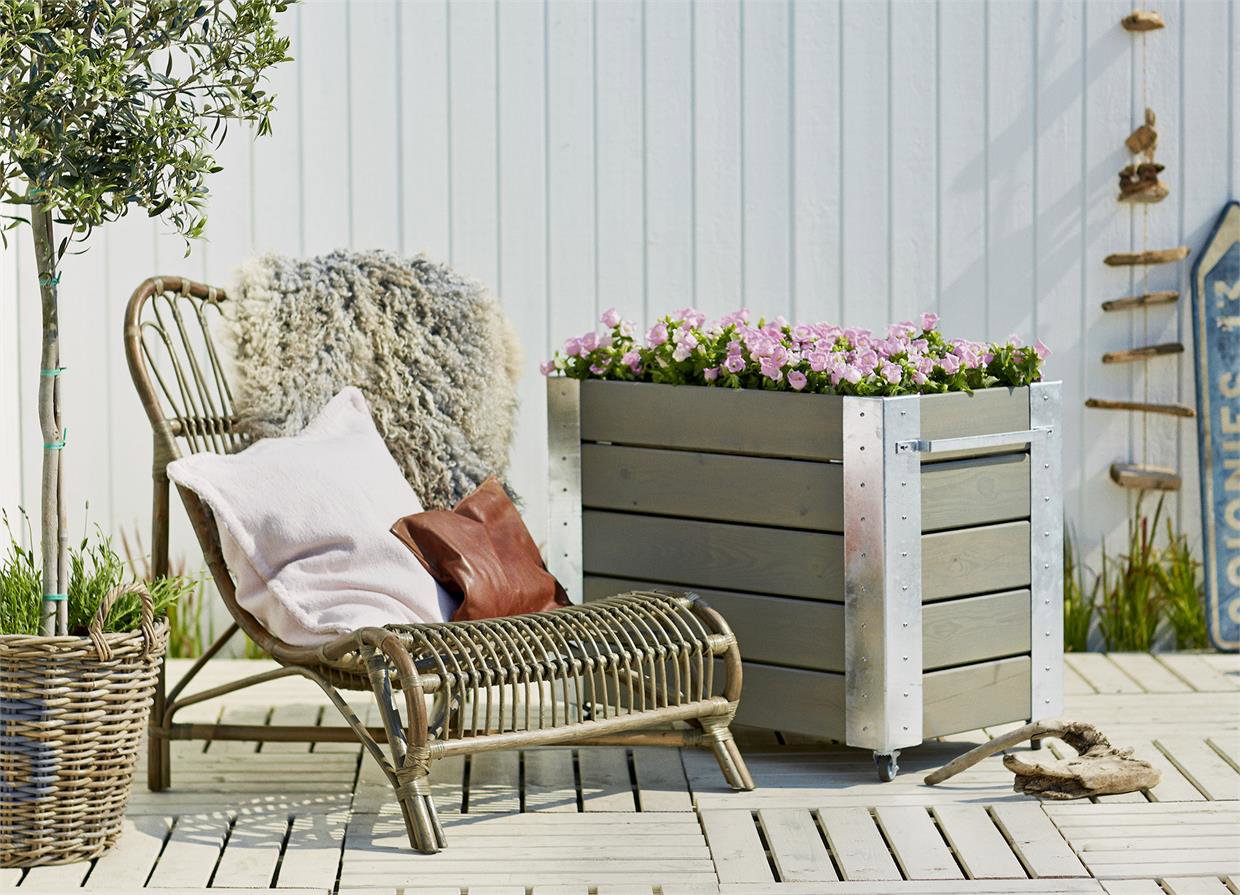 Haveindretning med lounge stol og plantekasse Terrasse med loungestol og stor plantekasse med blomster