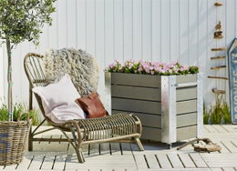 Haveindretning med lounge stol og plantekasse Terrasse med loungestol og stor plantekasse med blomster