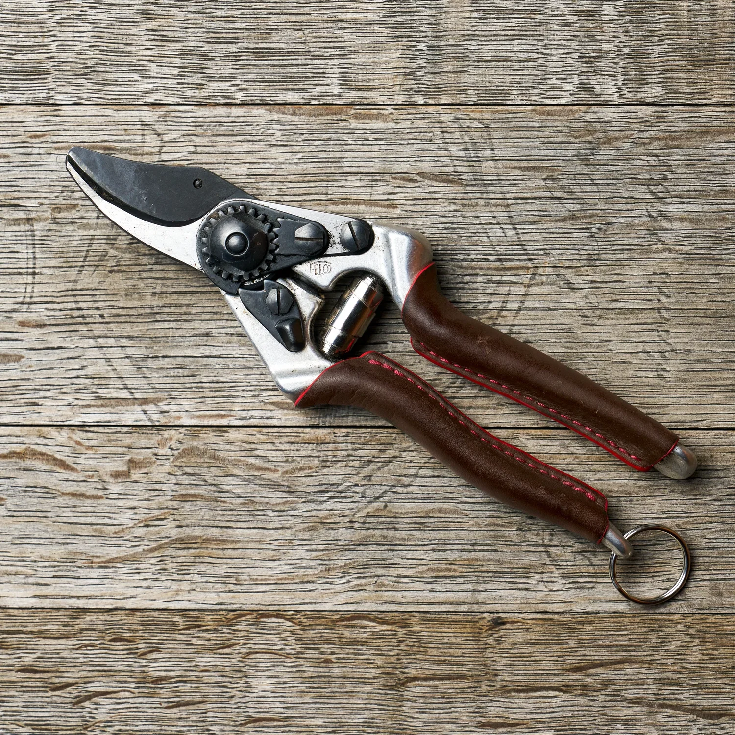 Felco 6 Elite beskæringssaks med F‑Tech sort belægning på klingen, ergonomiske brune håndtag med syning og ringlås, vist på træplanke — let og præcis beskæring