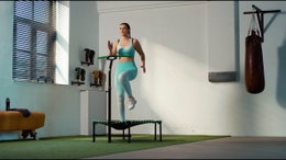 Salta Trampolin Fitness med håndtag - grøn | Salta Kvinde træner på Salta Trampolin Fitness med justerbart håndtag i grøn i et indendørs træningslokale – ideel til cardio, balance og styrkeøvelser