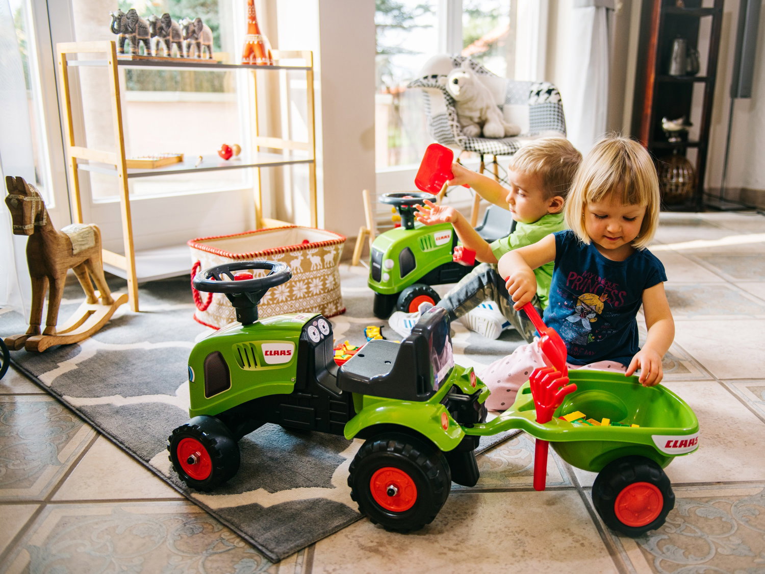 Små børn leger med grøn pedaltraktor med trailer