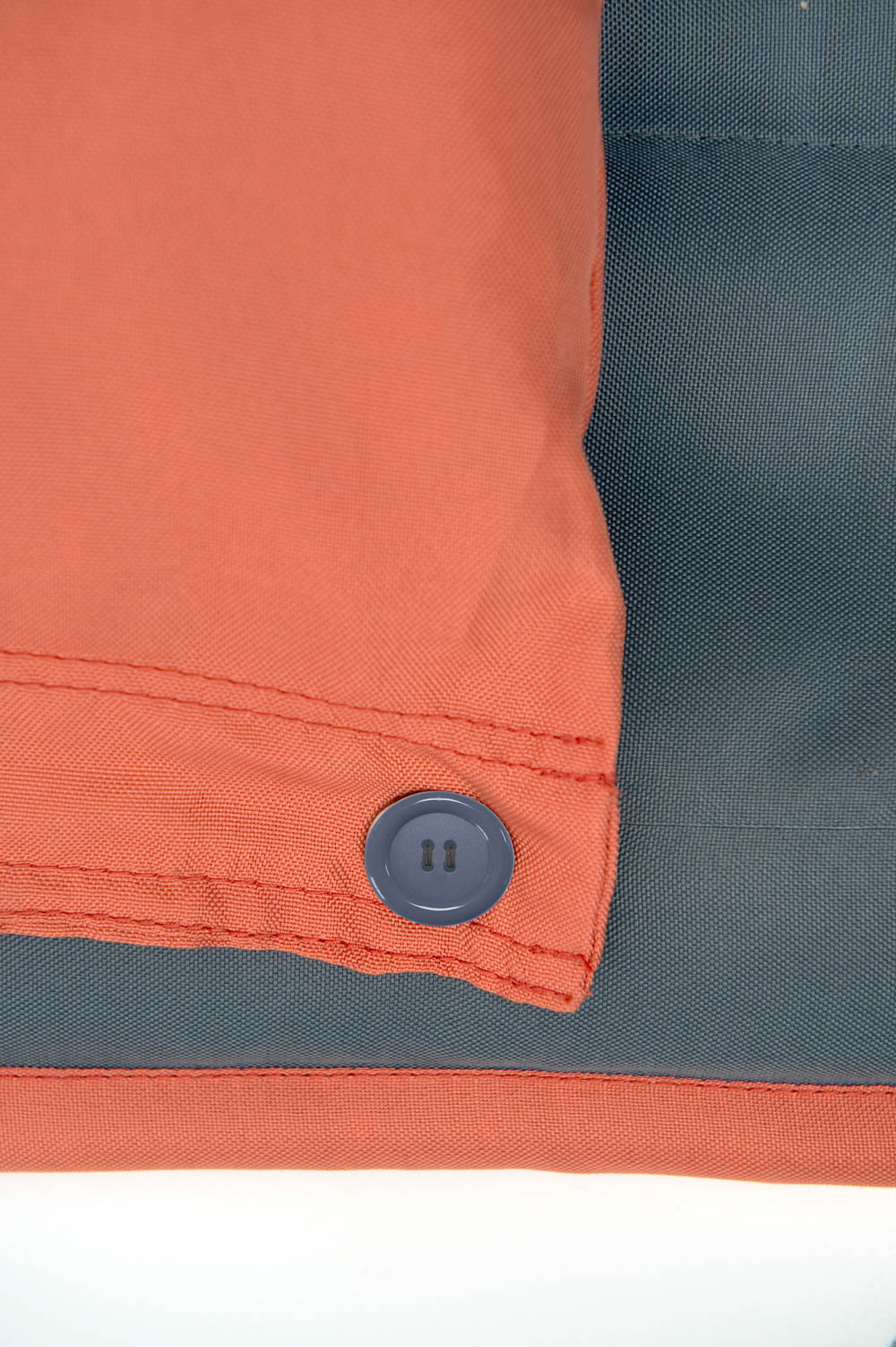 Detalje af orange pude med knaplukning Nærbillede af orange pude med grå knap