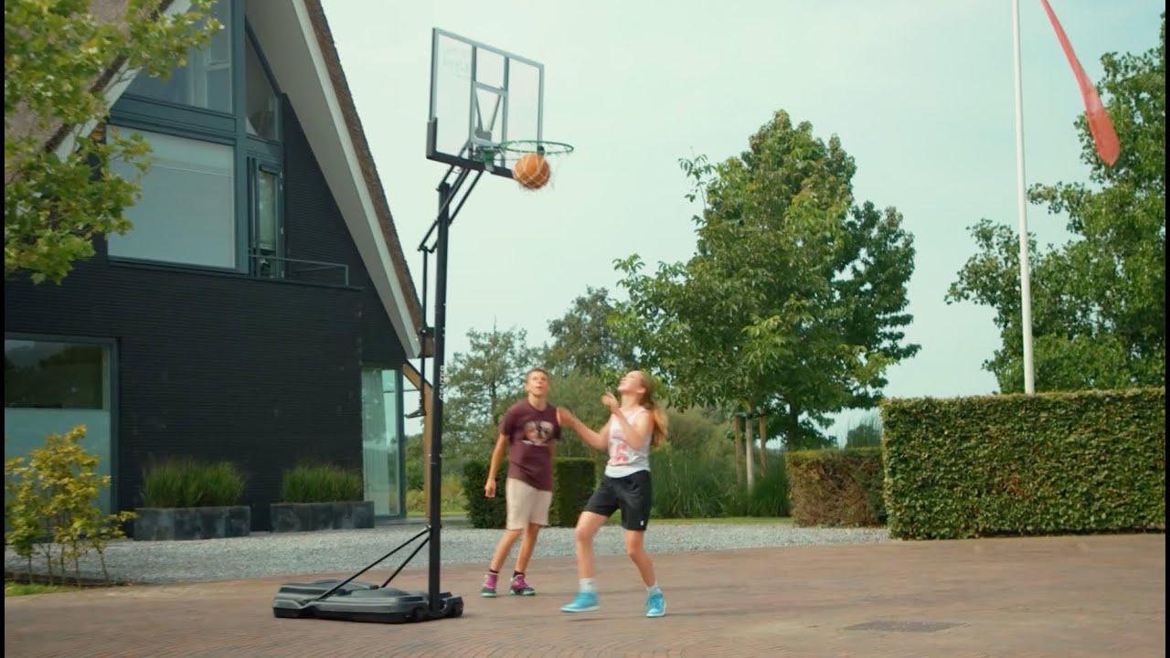 Salta Guard basketballstander 138 x 371 x 240 cm – robust polycarbonat bagplade, stålramme og dobbelte kompressionsfjedre til intensiv brug Salta Guard basketballstander med gennemsigtig polycarbonat bagplade og solid stålramme i indkørsel, to unge spiller basketball ved den justerbare stander (138 x 371 x 240 cm)