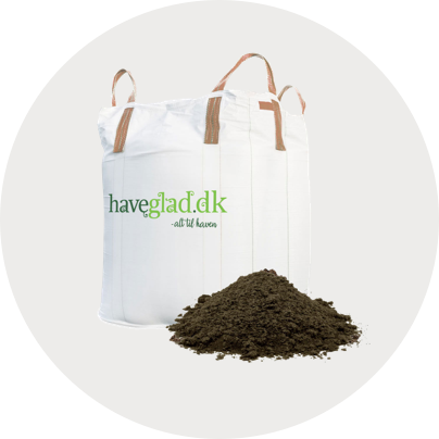 Hvid bigbag med grønne Haveglad.dk-logo og to bærehåndtag ved siden af en bunke løs havejord