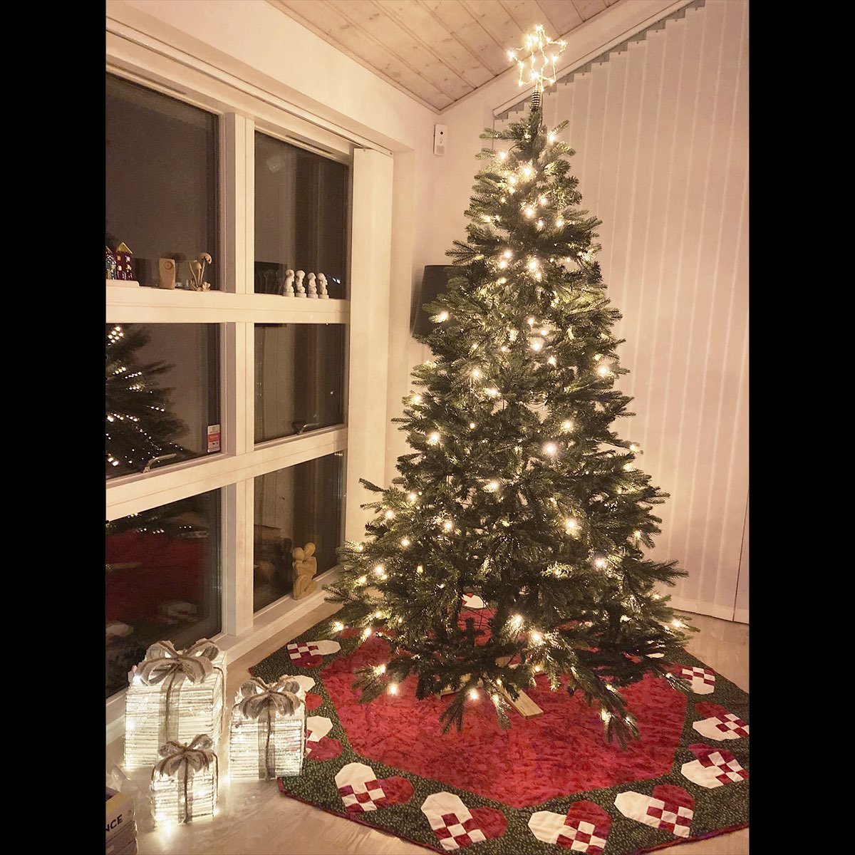 Højt juletræ med lys og juletræstæppe i stue
