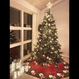 Opplyst juletræ i stue med julepynt Højt juletræ med lys og juletræstæppe i stue
