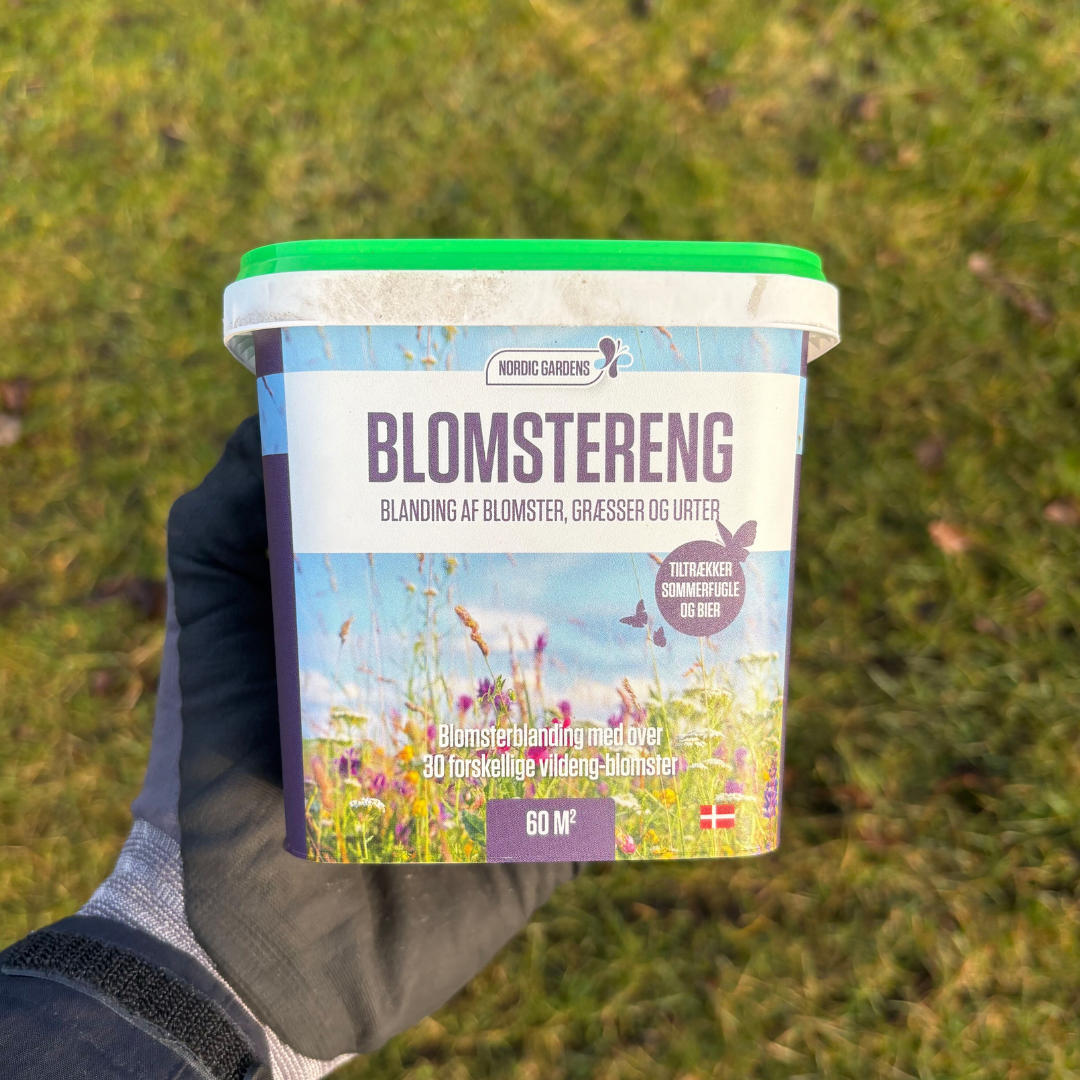 Beholder med Nordic Gardens 'Blomstereng' blomsterblanding til 60 m2, emballage viser tekst om blanding af ca. 30 et- og flerårige blomster, græsser og urter samt at den tiltrækker sommerfugle og bier