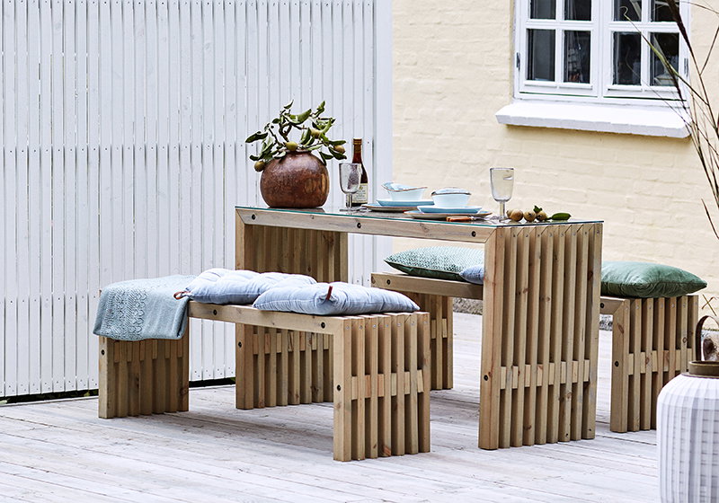 Moderne træbord med bænke og hynder på terrasse