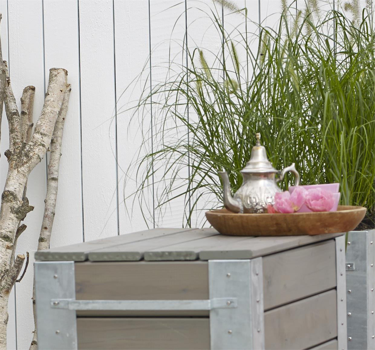 Havebord i træ med tekande og planter foran hegn