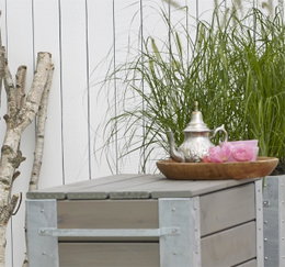 Havebord i træ med tekande og planter foran hegn