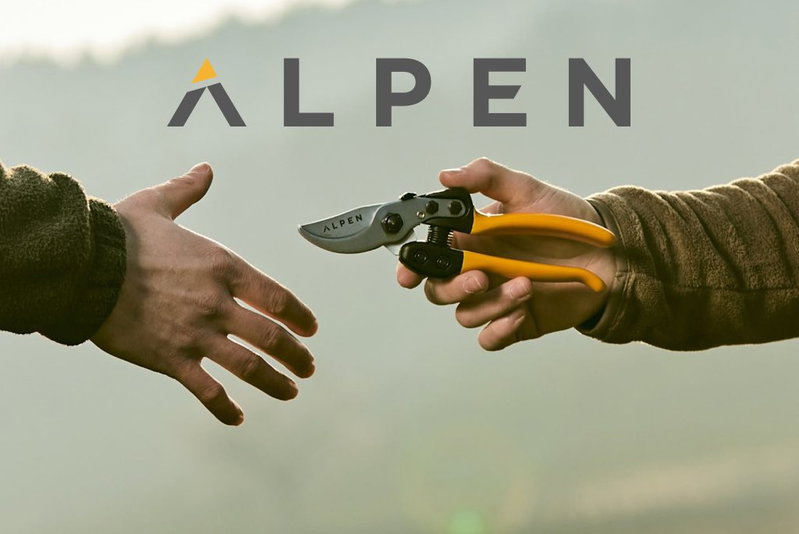 ALPEN beskærersaks med gule håndtag, to hænder udveksler værktøj foran sløret udendørs baggrund To hænder udveksler en ALPEN beskærersaks med gule håndtag; ALPEN-logo ses øverst, sløret naturbaggrund