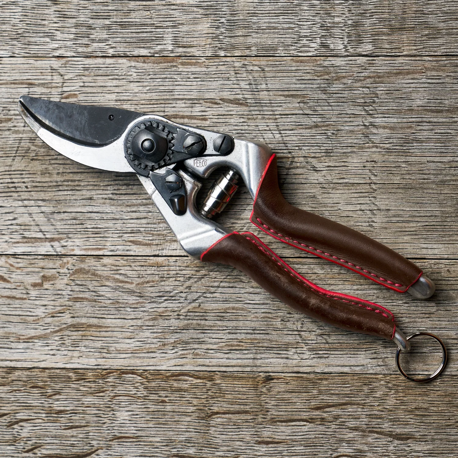 Felco 8 Elite beskæringssaks med vinklet skærehoved, sort F‑Tech belægning, ergonomiske brune greb og låsering på træbaggrund