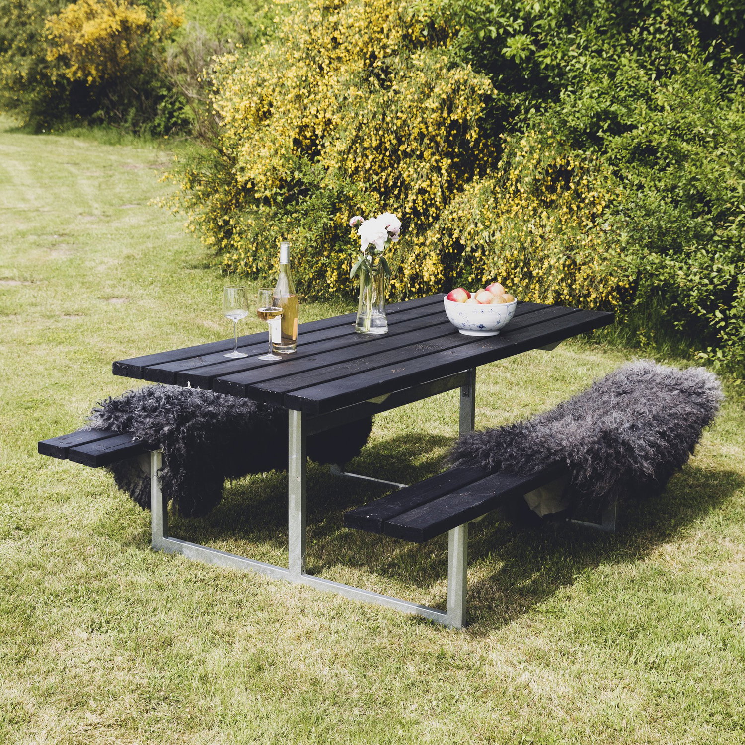 Sort picnicbord med bænke i have omgivet af buske