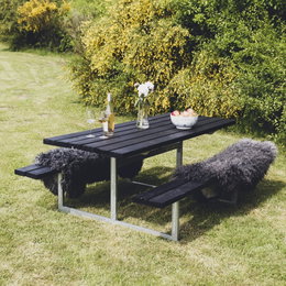 Sort havebord-bænkesæt i træ og stål Sort picnicbord med bænke i have omgivet af buske