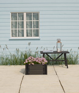 Udendørs sort plantekasse med lyserøde blomster Sort plantekasse med lyserøde blomster på træterrasse