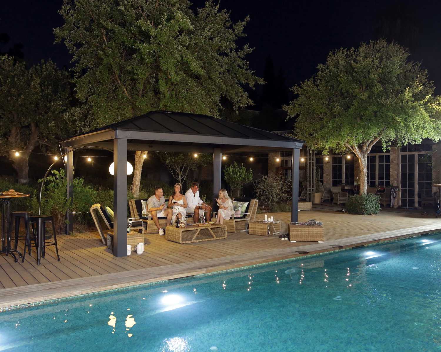 Havepavillon ved pool til hyggelige sommeraftener Moderne havepavillon med loungesæt ved oplyst pool