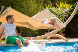 Par i hængekøje ved poolen i solen Afslappet par ved pool med hængekøje i træstel