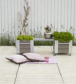 Hyggelig lys træterrasse med krukker og puder Lys træterrasse med plantekasser, blomster og puder på tæppe