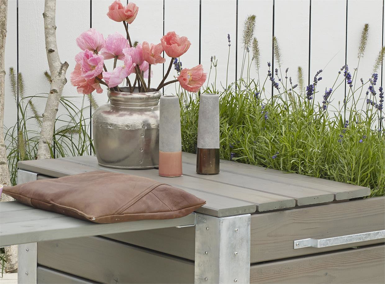 Gråt havebord med vase, lys og brun pude på terrassen