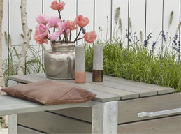Gråt havebord med vase, lys og brun pude på terrassen