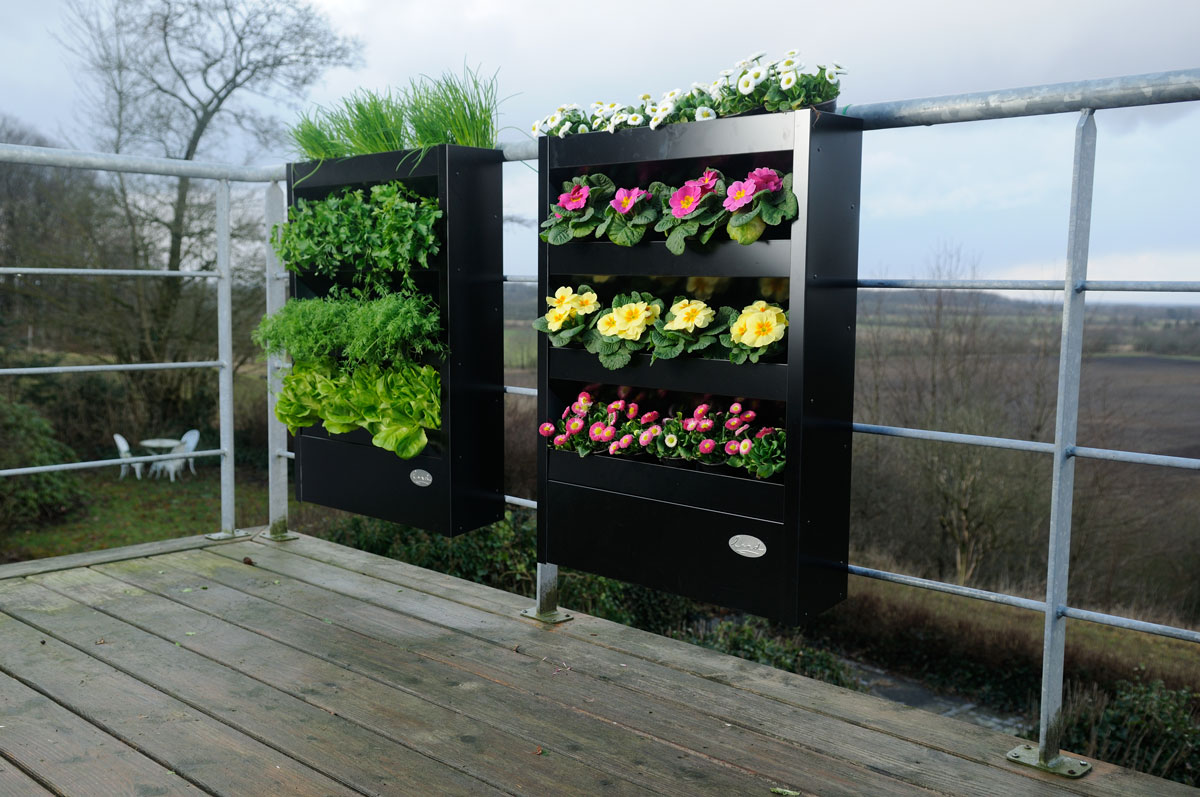 Lodret sort plantekasse med urter og blomster på altan