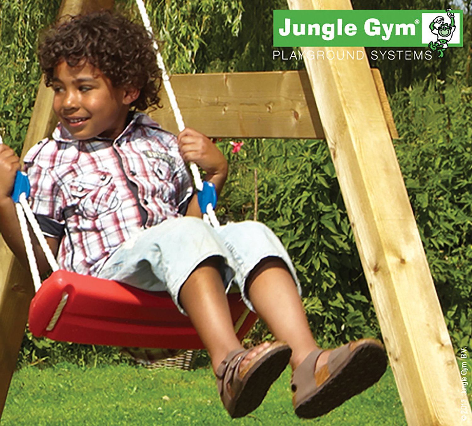 Barn gynger på Jungle Gym rød gynge Glad dreng gynger på rød Jungle Gym gynge